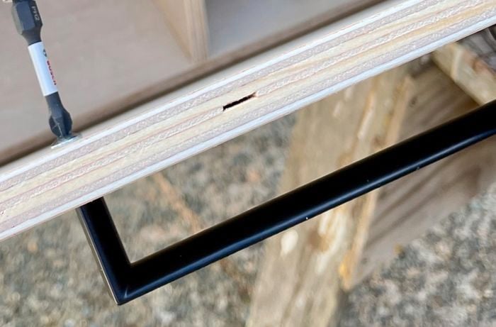 A wooden box with a black handle being attached to the side with a screwdriver