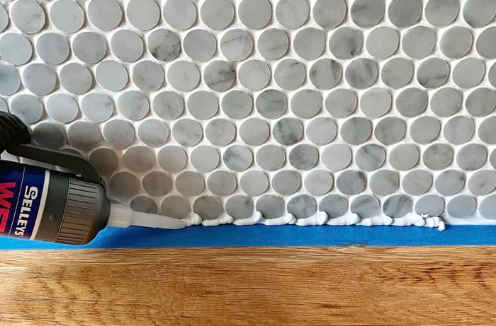 Silicone sealer is caulked between a bench and tiled splashback.