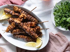  A white platter piled with chipotle chicken skewers with a bowl of rocket leaves on the side
