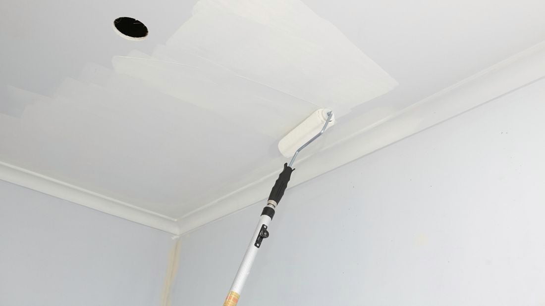 An extension roller being used to paint a ceiling with a cut-out for a light fitting