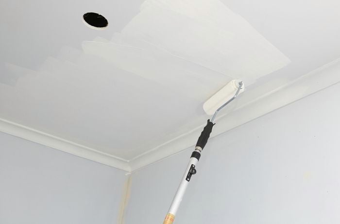 An extension roller being used to paint a ceiling with a cut-out for a light fitting
