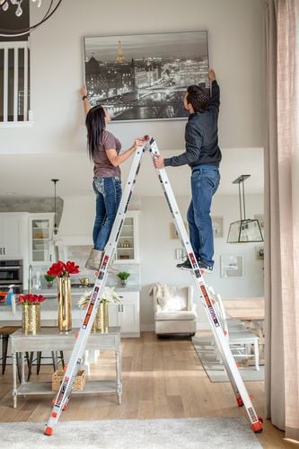 Two people standing on either side of ladder adjusting hanging picture