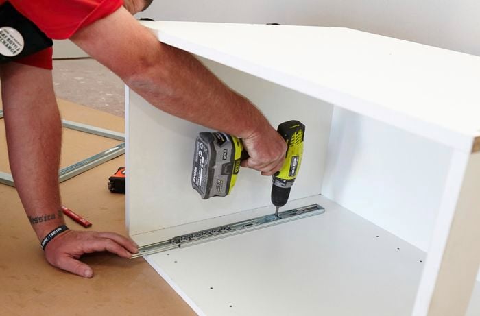 A Bunnings team member securing a basket rail to the bottom of a cabinet