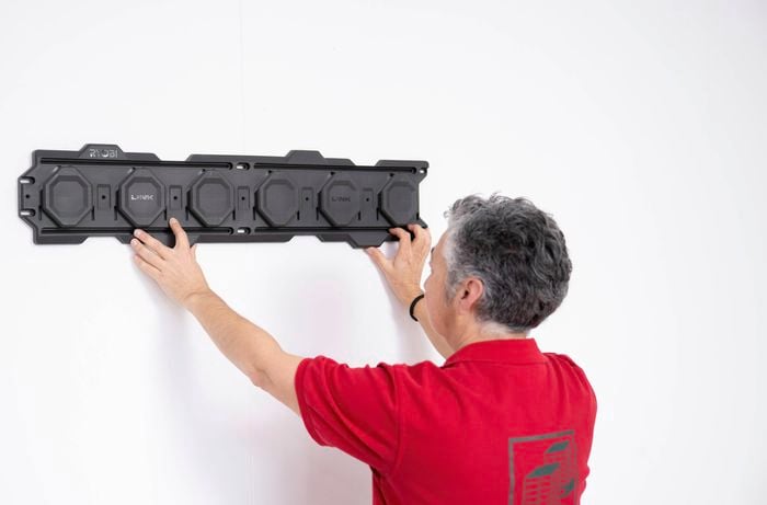 A Bunnings Team Member is positioning a Ryobi LINK rail system onto a white garage wall for installation.  