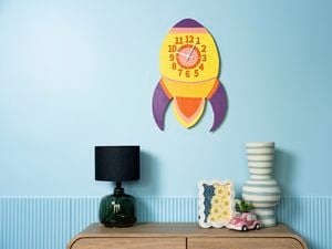 A colourful retro rocket wall clock displayed on a blue wall above a wooden console table with modern decorative pieces.