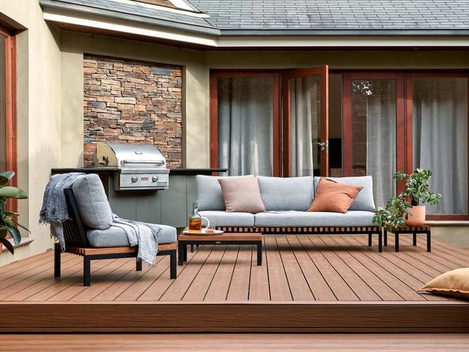 A Barbecue and outdoor setting on a timber decking with a cushion and pot plants on it.