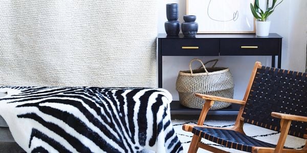 Zebra look rug draped over furniture, surrounded by black furniture and accessories with a black dog on a rug