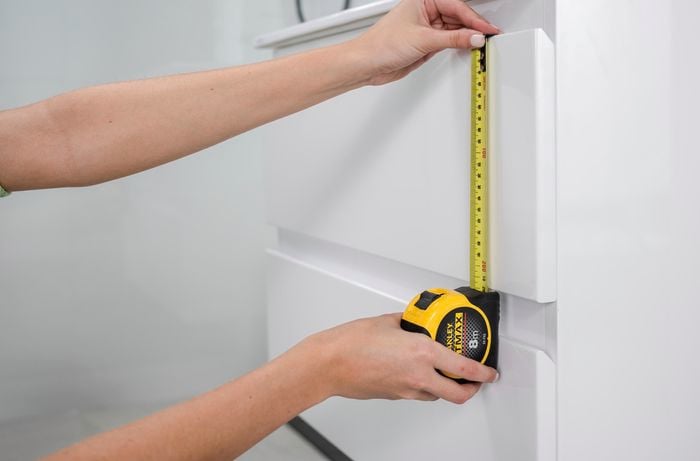 A tape measure being used to measure a white vanity