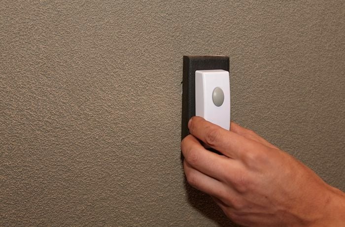 A person attaching a doorbell to a mount on an external wall