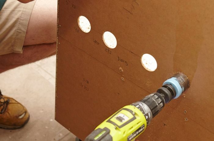 Cutting the pipe holes in the laundry cabinet with a hole saw.