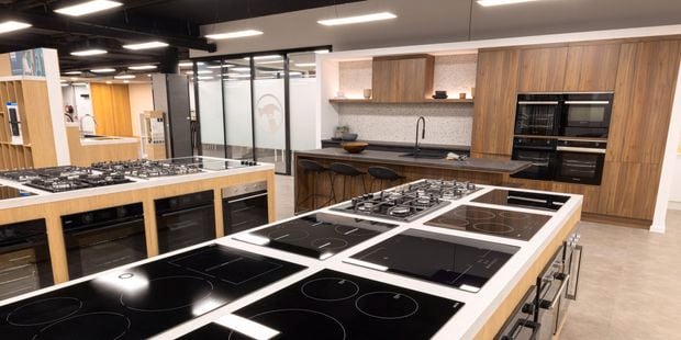 A kitchen display area with stovetops, ovens and a kitchen sink in it.