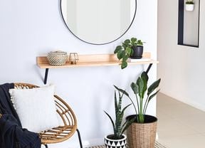 A round mirror, timber shelf, chair styled with throw and cushion and indoor plants in pots.