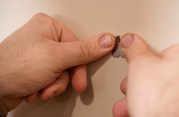 A person holding a claw picture hanger against a wall