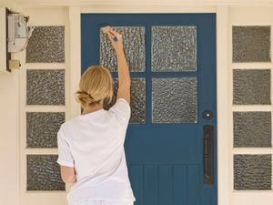 A woman in a white t-shirt painting a blue front door.