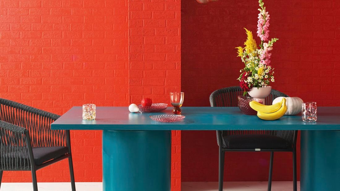 Fruits and a flower vase on top of a green table in a living room.