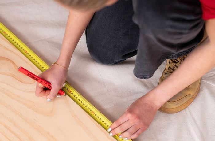 A person marking measurements on a timber board