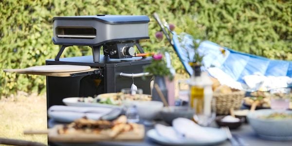 View of a Cozze pizza oven behind a table set with food.