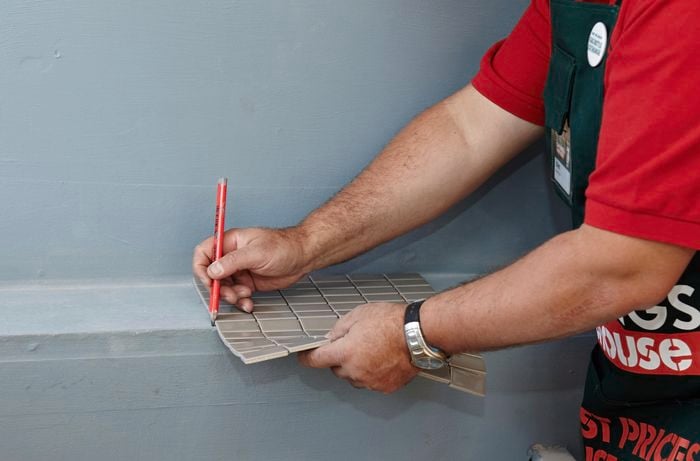 A sheet of mosaic tiles being used to mark a wall for tiling with a pencil