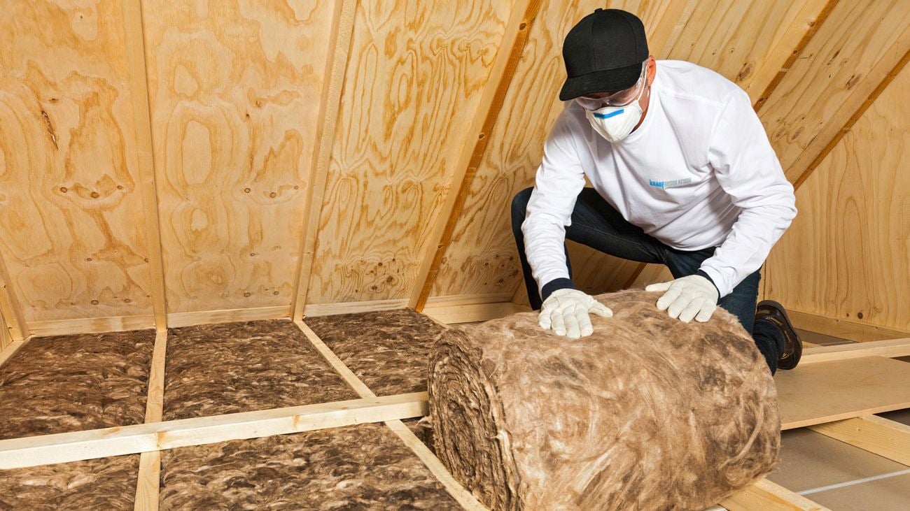 Man rolling insulation wool into walls of a house.