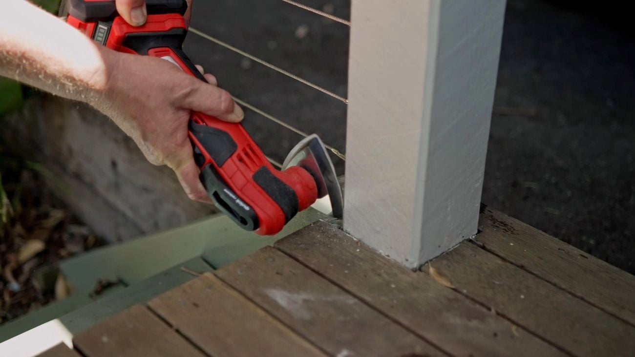 A pair of hands holding a multifunction tool with sanding head to sand back outdoor timber steps