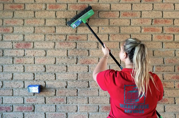 A Bunnings Team Member is using stiff bristle broom to clean brick wall
