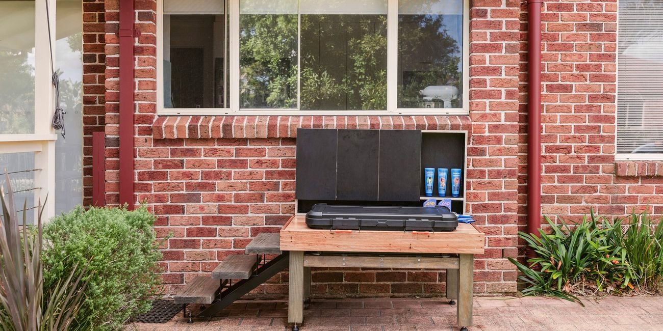 A raised wooden dog-wash station with steps and open storage shelves sits against a brick house wall beneath a window.