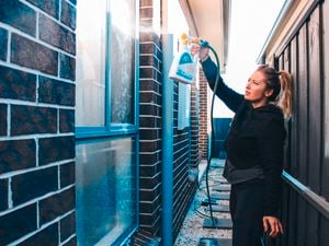A woman holding the 30 seconds outdoor cleaner attached to a hose and spraying the liquid onto a window on the side of a house.