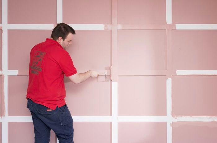 A Bunnings Team Member is using a paint roller to apply pink paint on the installed battens.  