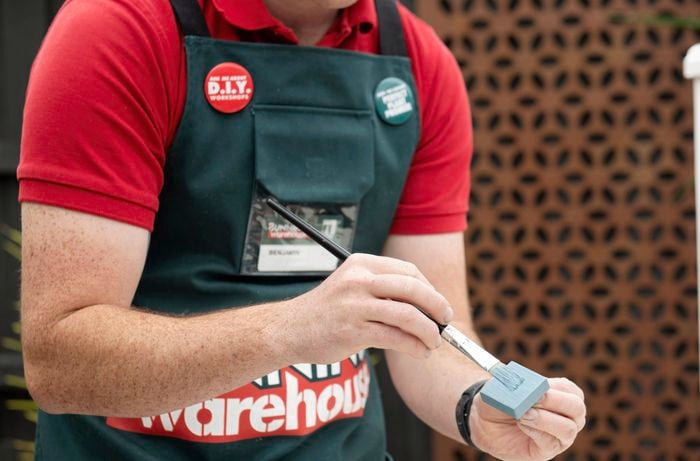 A square toggle being painted pale blue by a Bunnings team member with a paintbrush