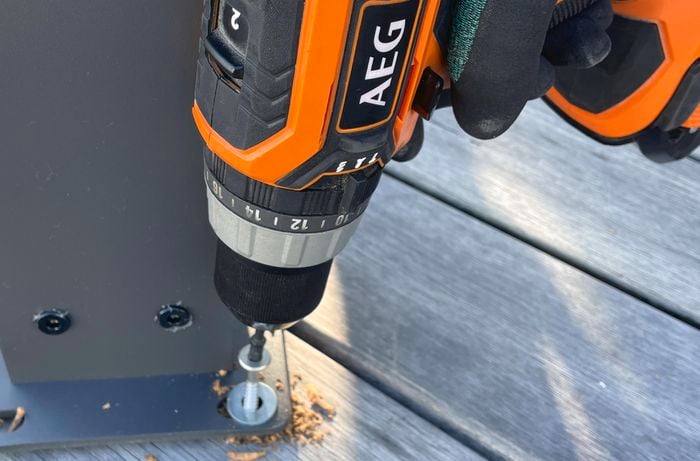 Person bolting base plates of a gazebo to an outdoor deck with a drill.