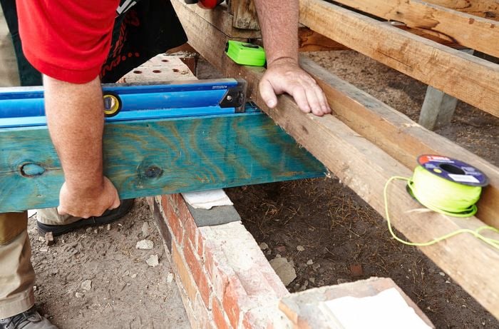 A person lifting a bearer onto some packing sitting on a course of bricks