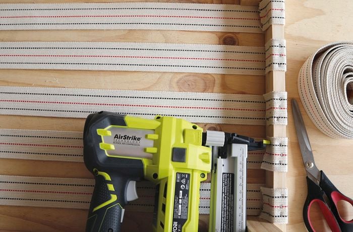 Person using nail gun to attach cloth to timber frame