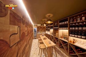 A bar area with lot of bottles of wine in it with a table and stools around it.
