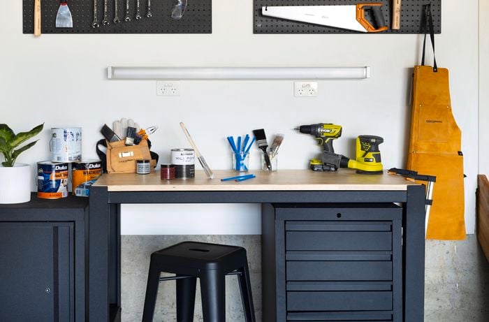 A black workbench with timber benchtop, a matching lockable cabinet and small tools hung on a black pegboard