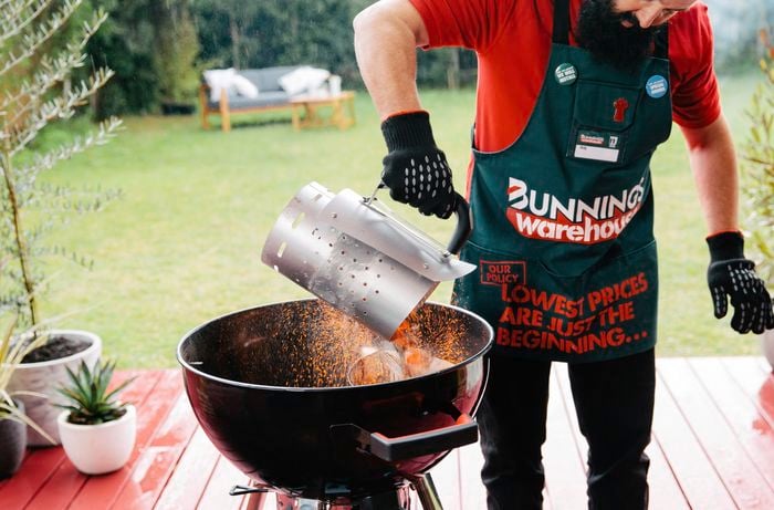 Person pouring hot charcoal briquettes into a smoker