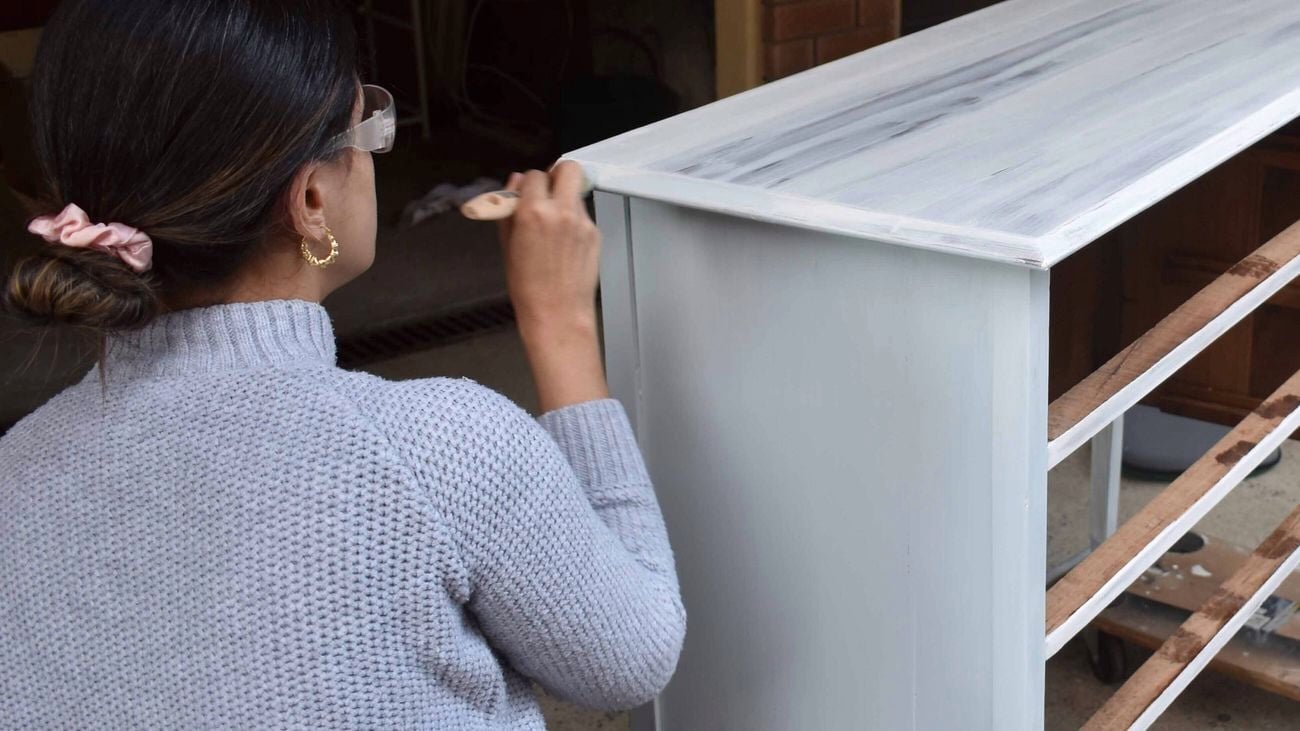 A woman painting a white dresser using Porters Revive Furniture Paint.