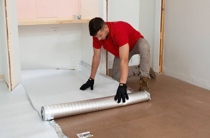 A Bunnings Team Member is laying underlay on the floor in a room.