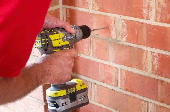 Person drilling a hole in a brick wall with a cordless drill