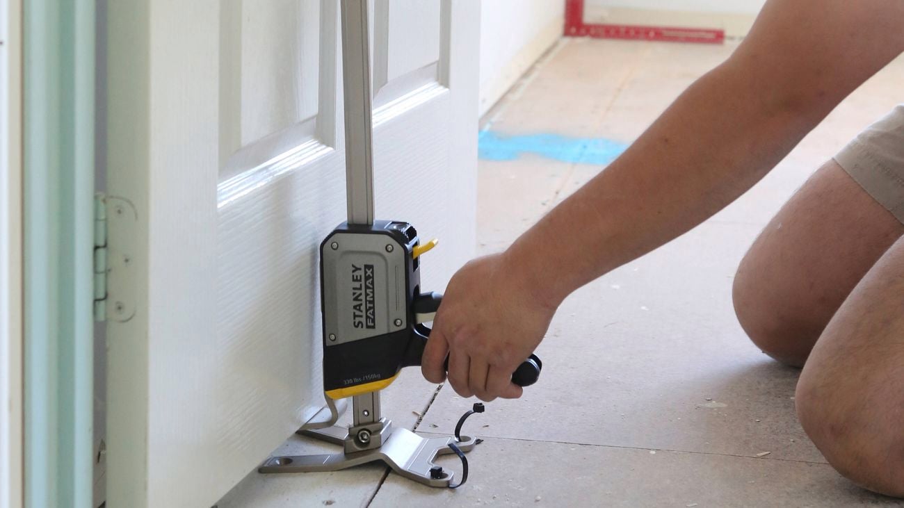 A close up image of a hand holding a Stanley FatMax Tradelift in place underneath a door frame.]