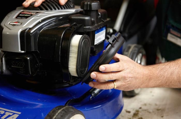 A person removing the cover from the air filter on a lawn mower 