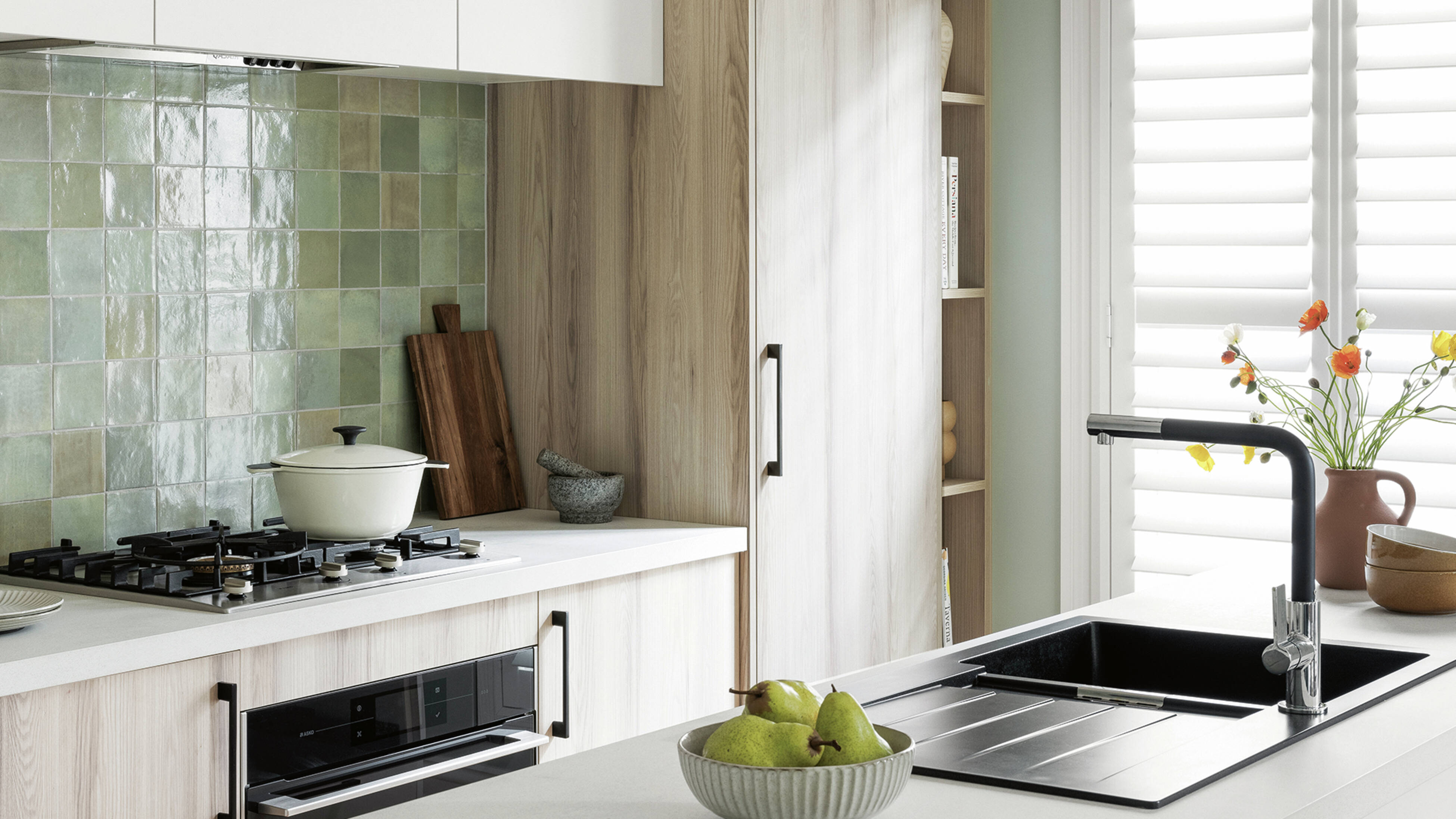 A modern kitchen featuring a sleek black sink, natural wood cabinetry, and a green tile backsplash for a tiling trend in a contemporary look.