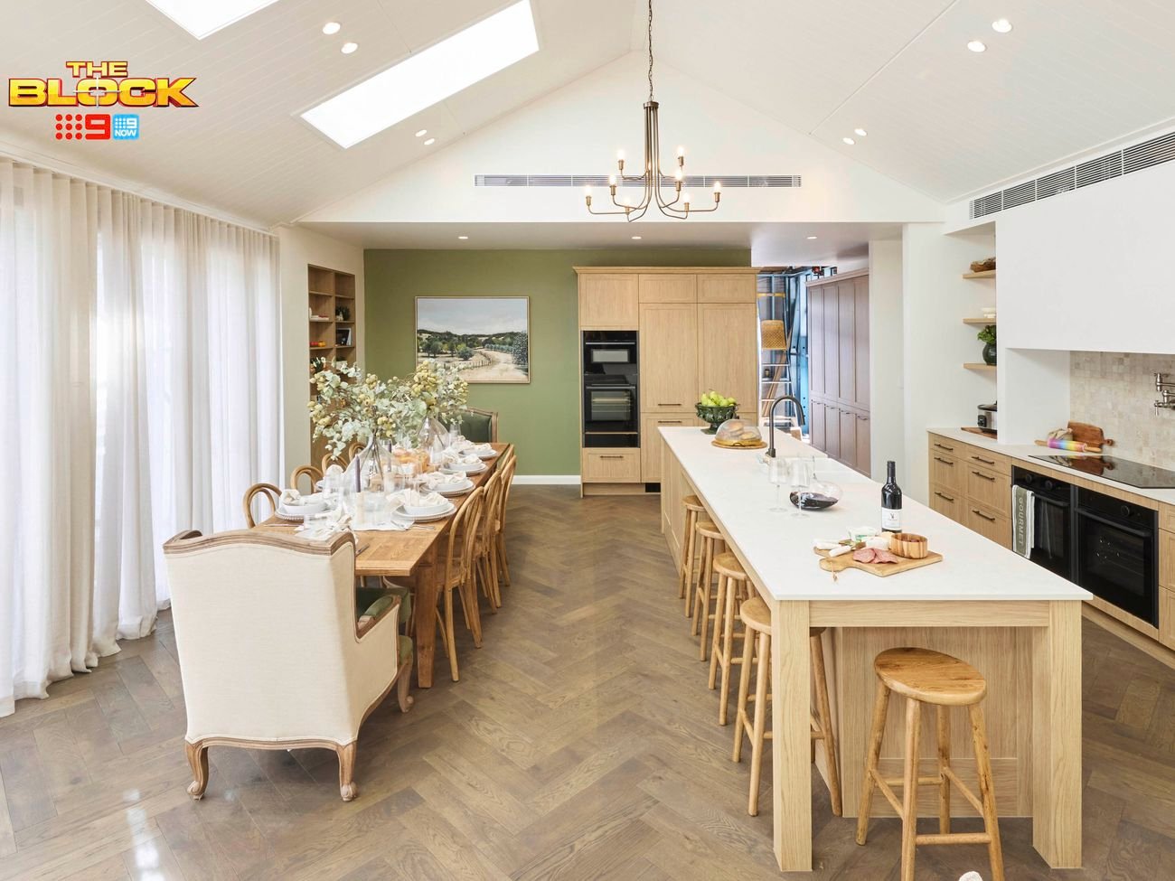 Kitchen with long island, wooden stools, and dining table by large windows.
