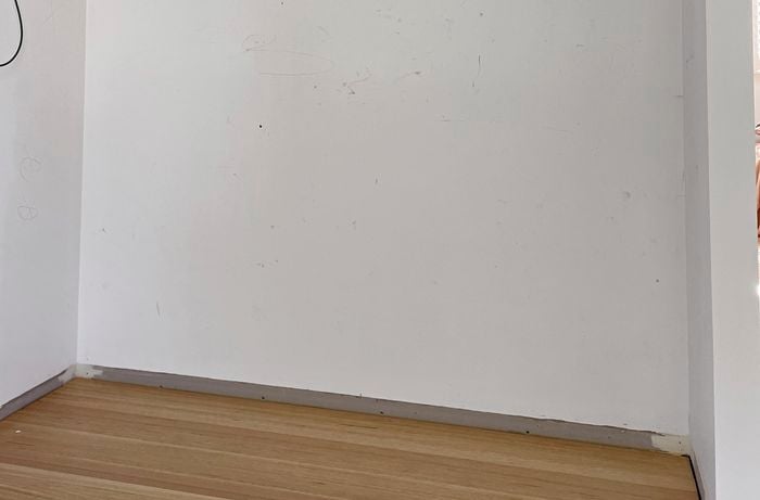Room with floorboards, white wall and nothing in it