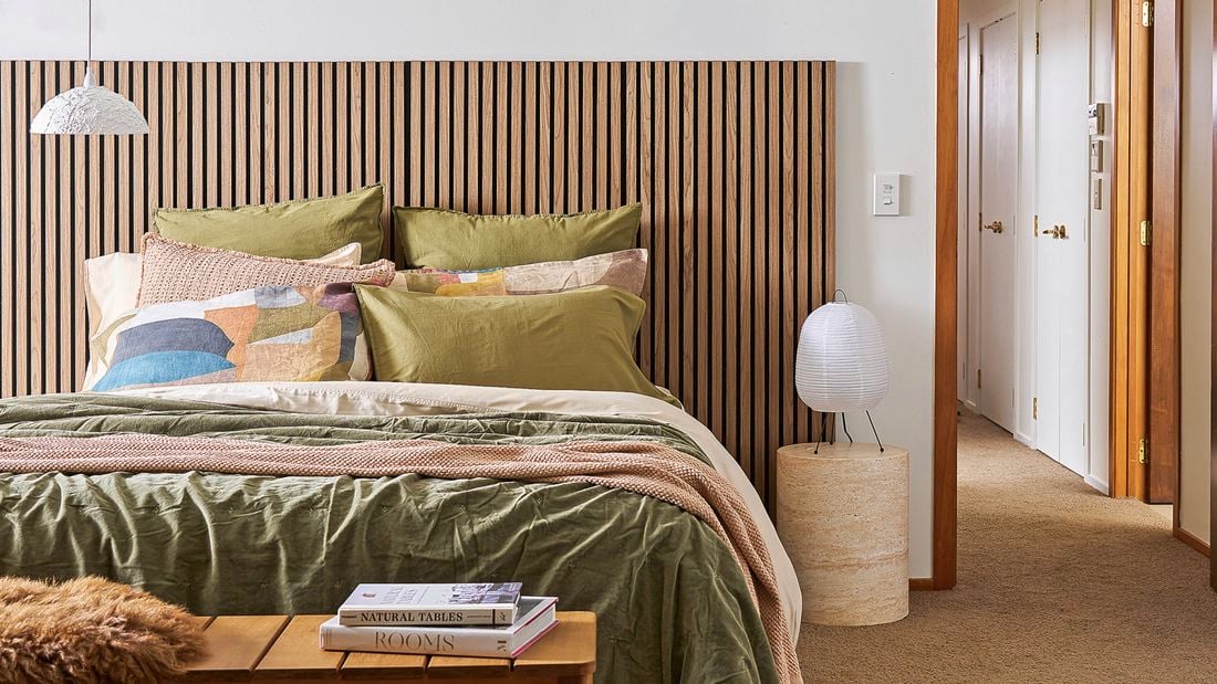 A bedroom showing a bed with a timber headboard, cosy blankets and pillows to help with home insulation