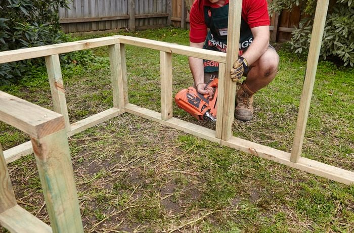 A wooden frame being assembled on a workbench by a Bunnings team member with a nail gun as part of a chicken coop