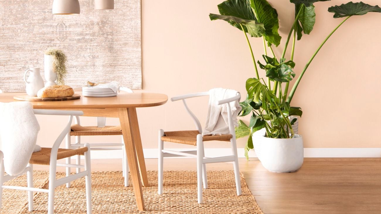 Oak dining table and white dining chairs in a calm and neutral dining room featuring a rug hung on a wall.