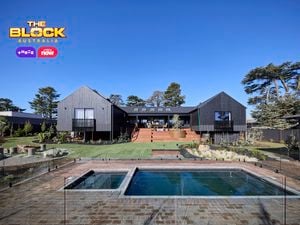 The back of a house with a pool in it, a rocked area, timber decking and many plants in it.