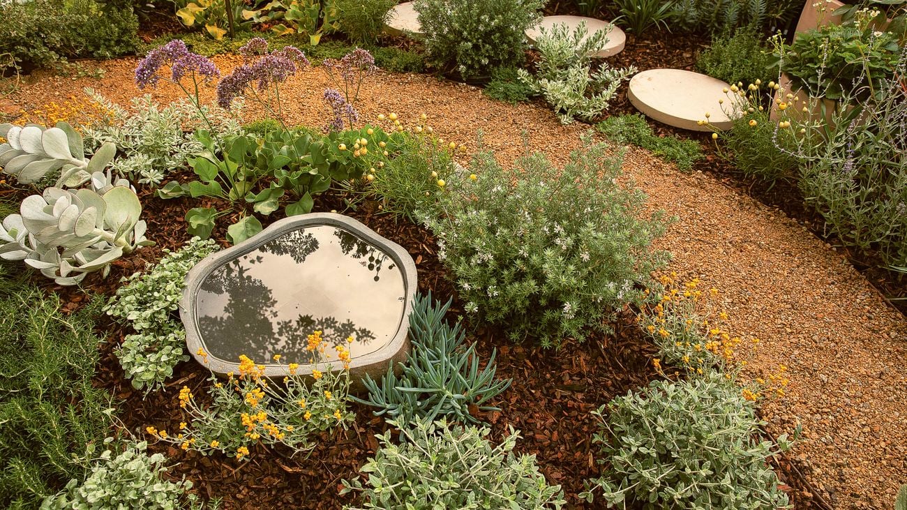 Curved gravel garden path with lush plantings and a water feature.