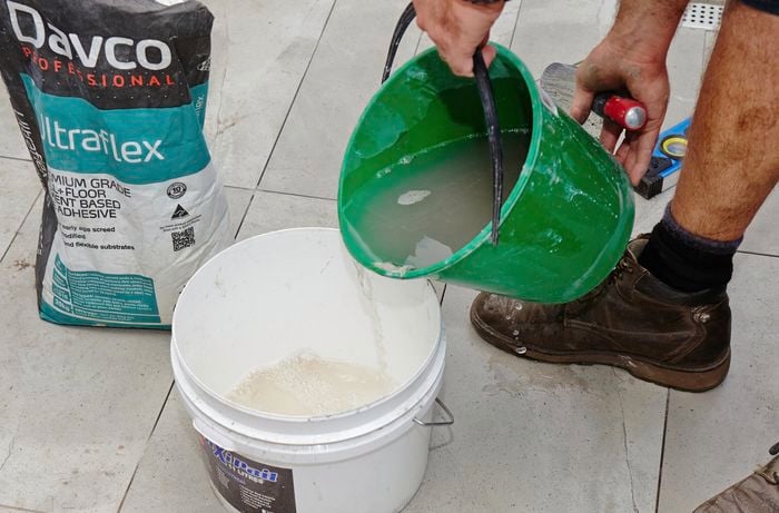 A person pouring water into a mixing bucket containing powdered adhesive