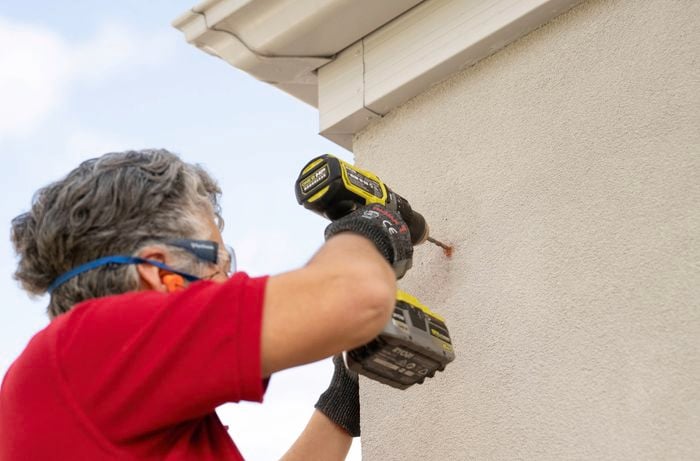 A person is drilling into the marked holes to get the wall ready for mounting a Swann security camera.